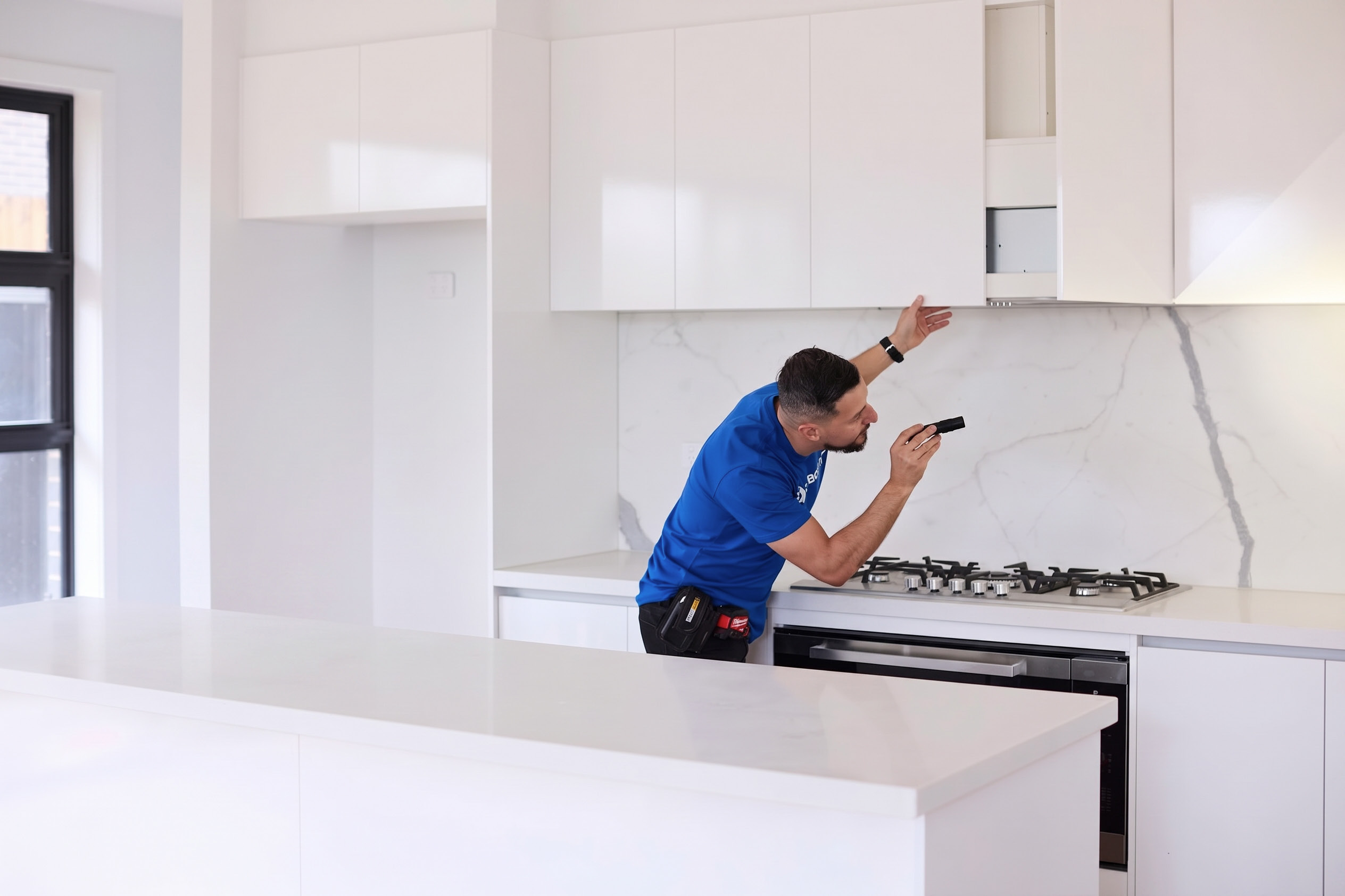 Building inspector using a torch to examine kitchen cabinetry